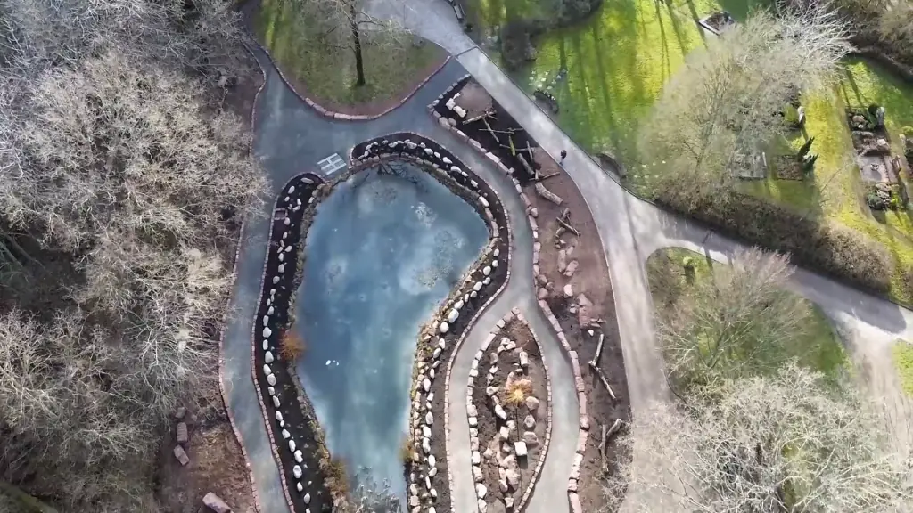 Luftaufnahme von oben: Teich mit Steinufer, geschwungene Wege und Grabfelder zwischen Bäumen
